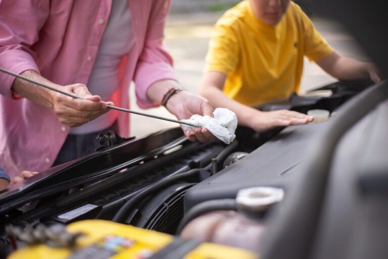 Father and son working on car maintenance, checking engine oil outdoors.