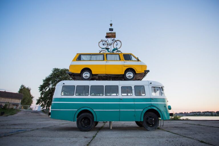 Creative outdoor sculpture featuring a van stacked on a bus with a bicycle on top.