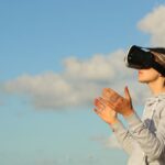 Woman using VR headset outdoors, exploring virtual reality under a clear blue sky.