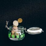 Glass jar with coins falling into it on a black background, symbolizing savings.