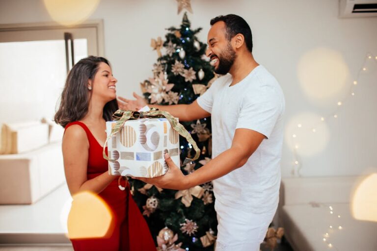 A happy couple exchanges Christmas gifts by a decorated tree indoors, full of festive cheer.