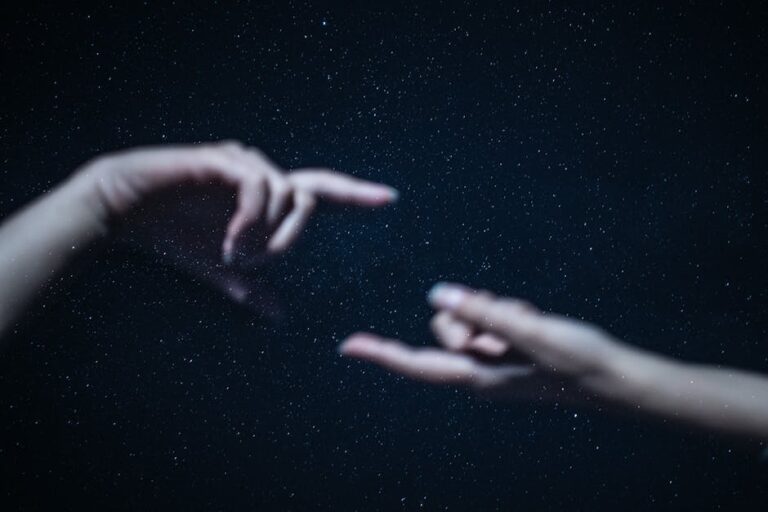Artistic depiction of two hands almost touching against a backdrop of a starry night sky.