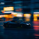 A sleek black sports car zooms through a vibrant city street at night.