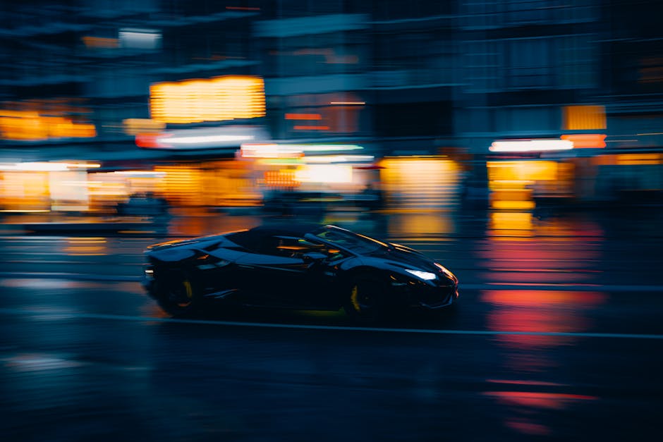 A sleek black sports car zooms through a vibrant city street at night.