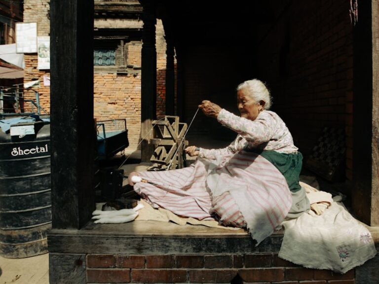 Senior woman weaving yarn with traditional tools on a sunny outdoor terrace.