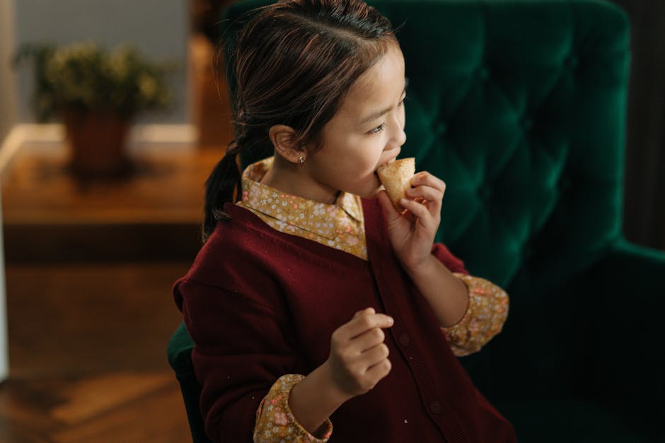 Young girl with ponytail enjoying a baked snack in a cozy indoor setting, capturing moments of childhood joy.