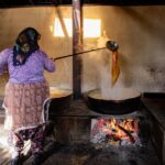 An adult woman making traditional sweets over an open fire in a rural village kitchen.