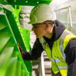 A worker in a safety vest and helmet inspecting industrial machinery.