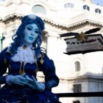 Event actor in blue costume with floating book in historical cityscape.