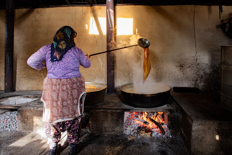 An adult woman making traditional sweets over an open fire in a rural village kitchen.
