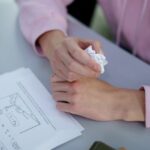 Close-up of a student's hands holding crumpled paper next to exam sheets on a desk.