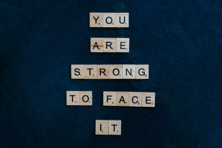 Scrabble tiles spelling 'You Are Strong To Face It' on a dark surface, conveying empowerment.