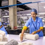 Indian textile worker organizing fabric rolls in a factory setting.