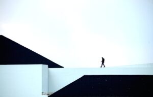 Silhouette of a person walking on a geometric architectural structure under a vast sky.