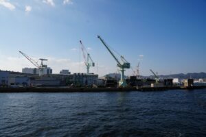 View of cranes at Kobe port under a clear blue sky, showcasing Japan's industrial capabilities.