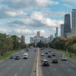 View of Chicago skyline with traffic on a tree-lined road under a cloudy sky.