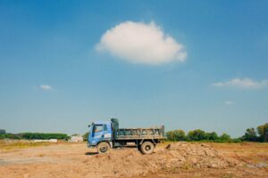 A blue truck parked on a construction site under a bright blue sky with scattered clouds.