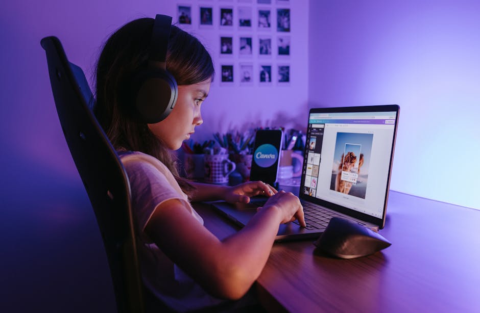 A young girl using a laptop with headphones in a dimly lit room, focusing on creative technology.