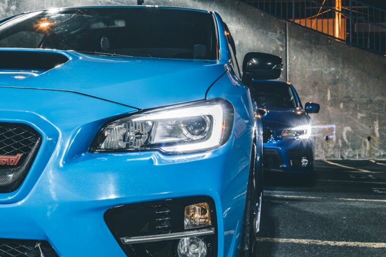 A vibrant blue sports car with headlights on, captured in a modern street setting during the night.