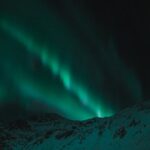 Majestic aurora borealis illuminates the night sky over snow-covered mountains.