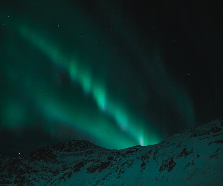 Majestic aurora borealis illuminates the night sky over snow-covered mountains.