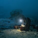 A solitary miner with headlamp gathers sulfur in baskets at a quarry during night.