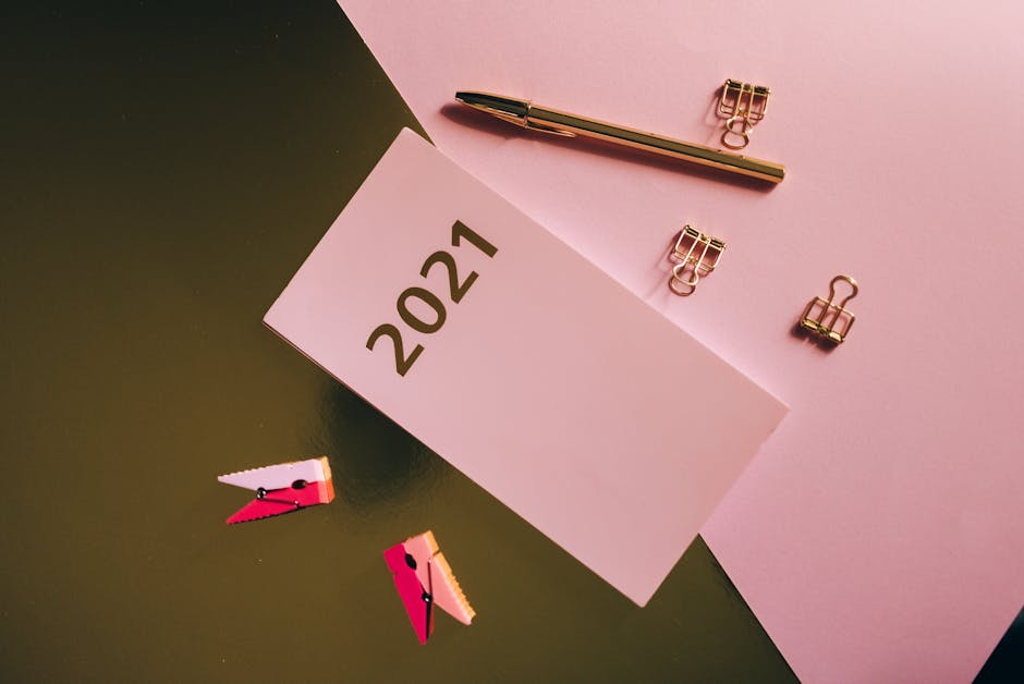 Flat lay of office supplies including a 2021 calendar card, pen, and clips on a pink background.