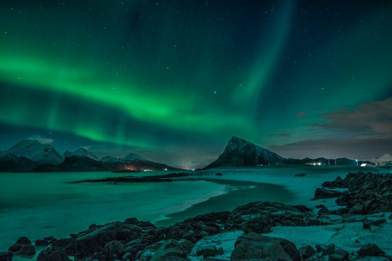 Stunning display of the Aurora Borealis illuminating the snow-covered coast and mountains in Nordland, Norway at night.