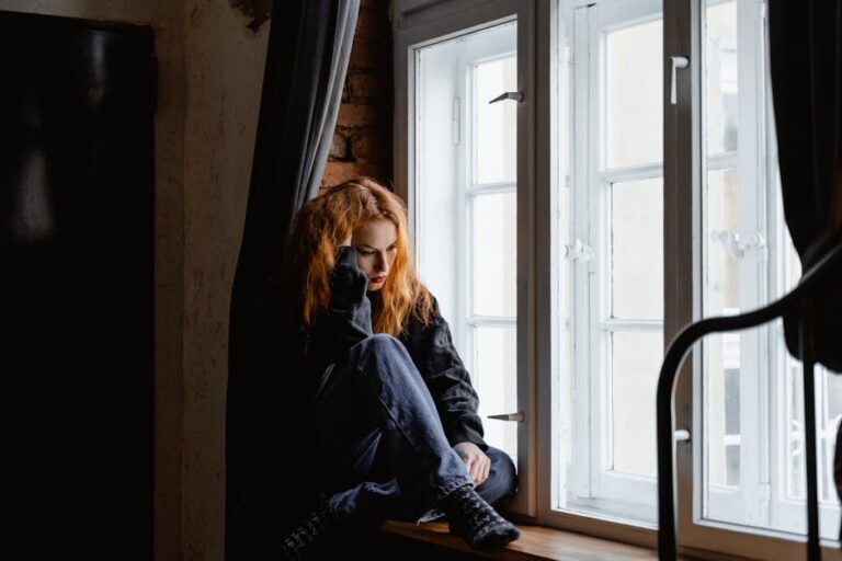 A woman sits by a window, lost in deep thoughts and moody light.